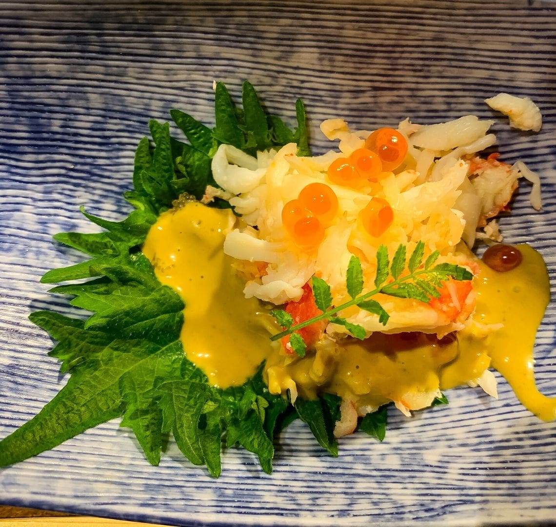 5 reasons to go family skiing in Niseko Wanderlust Family - a delicious starter of tiger prawn with cod roe on a yuzu leaf with yellow sauce all on a blue and white Japanese style plate