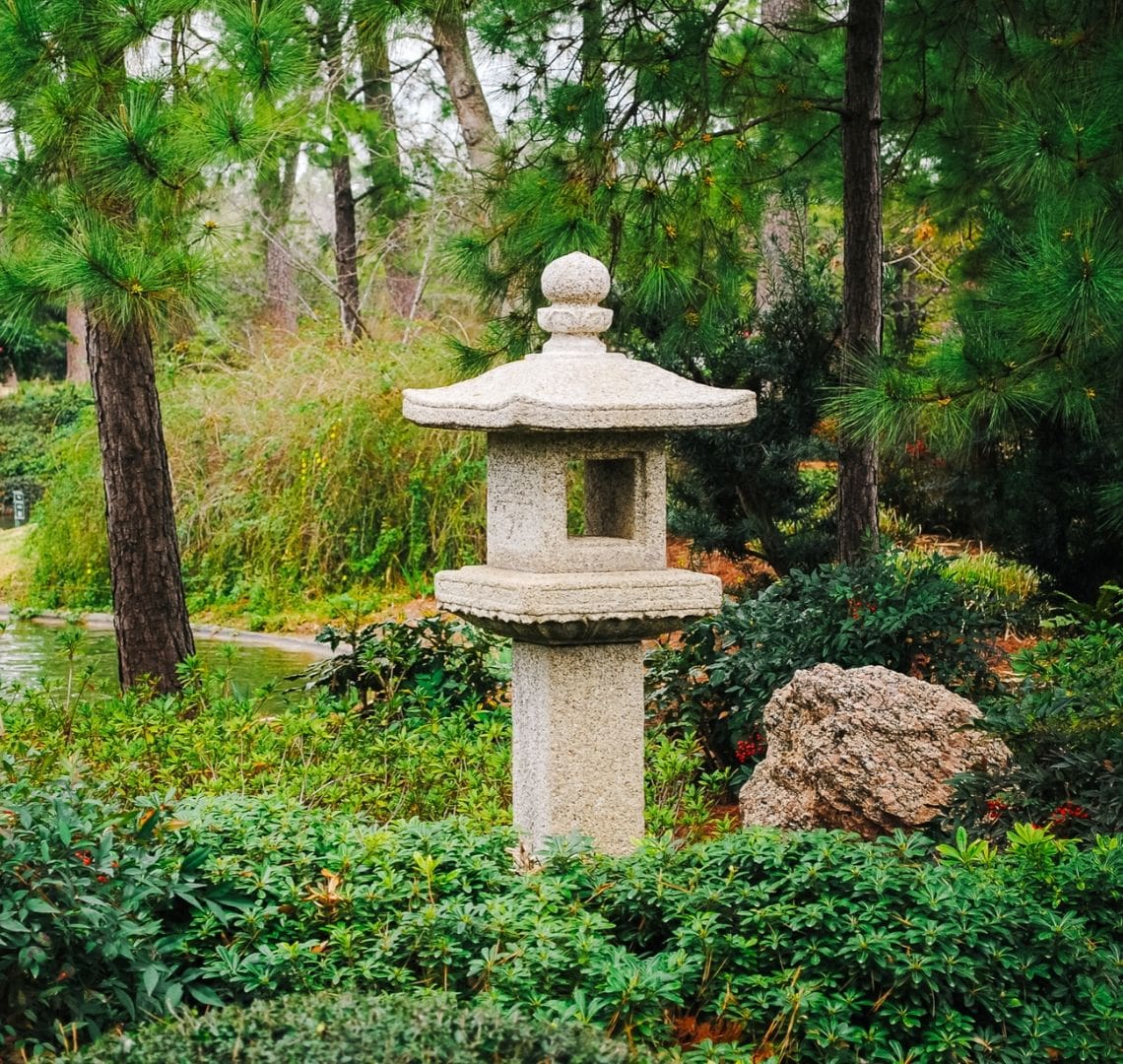 Things To Do In Houston With Kids - a stone bird table in the Japanese Gardens in Hermann Park. The background and foreground are all green (trees, grass, etc)
