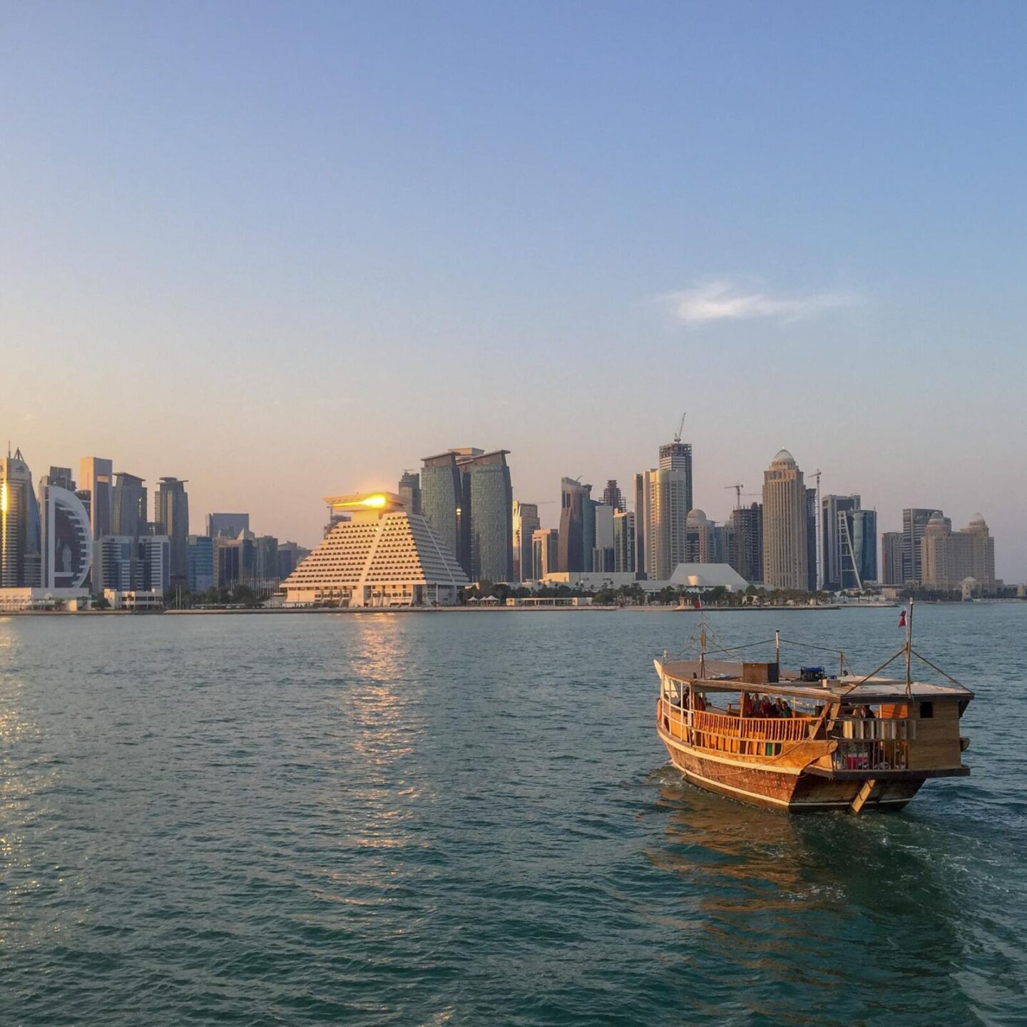 Qatar One Year On - Doha skyline at dust with a dhow boat in the aqua waters on the right