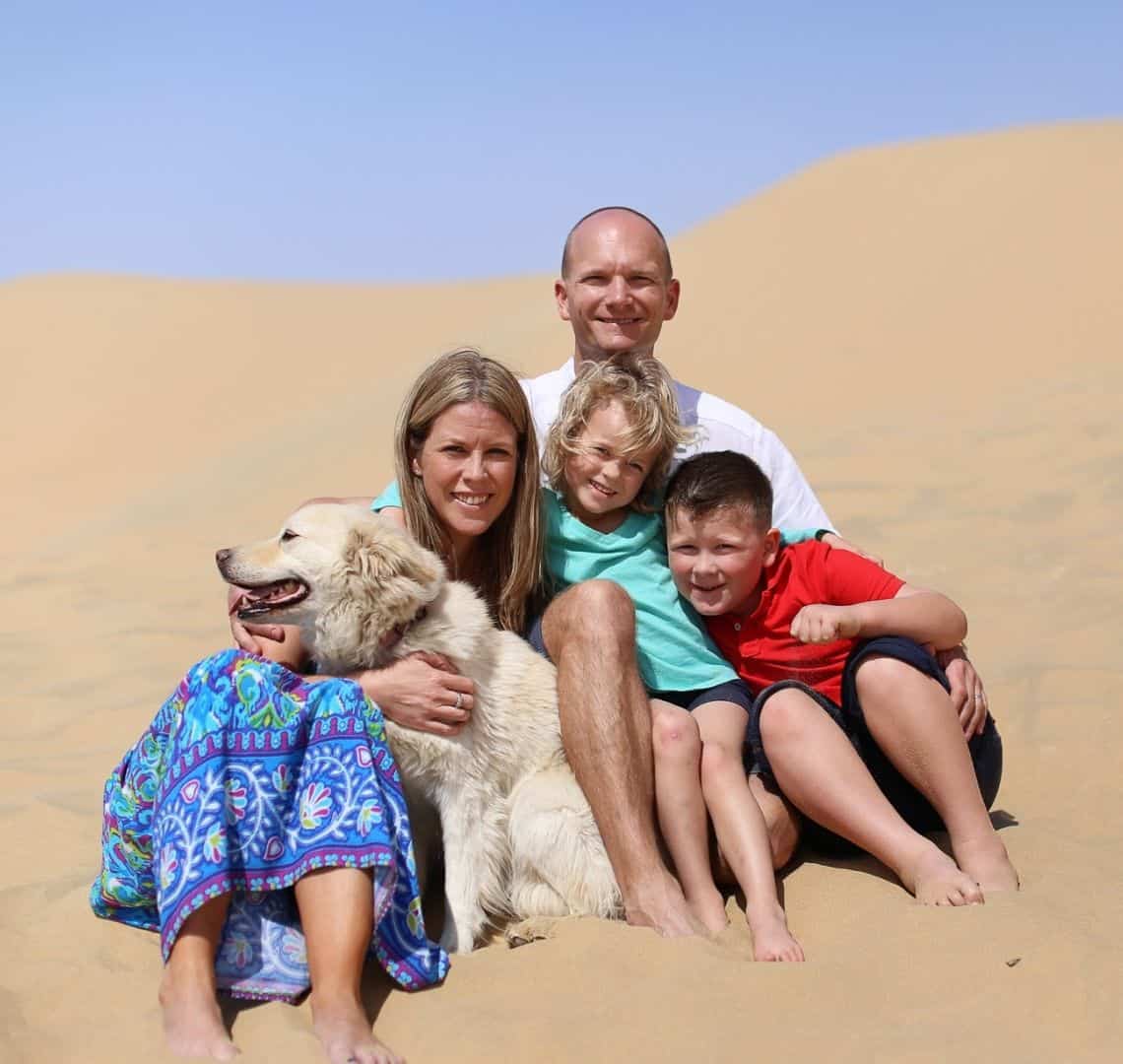 From left to right - me in ablue dress, Doggy Wanderlust (think retriever mongrel), Mr Wanderlust (behind) in a white shirt, Thing 2 on his lap in a turquoise/aqua t-shirt and Thing 1 in a red polo next to them. We are sat on a yellow sand dune and the sky is bright blue. 